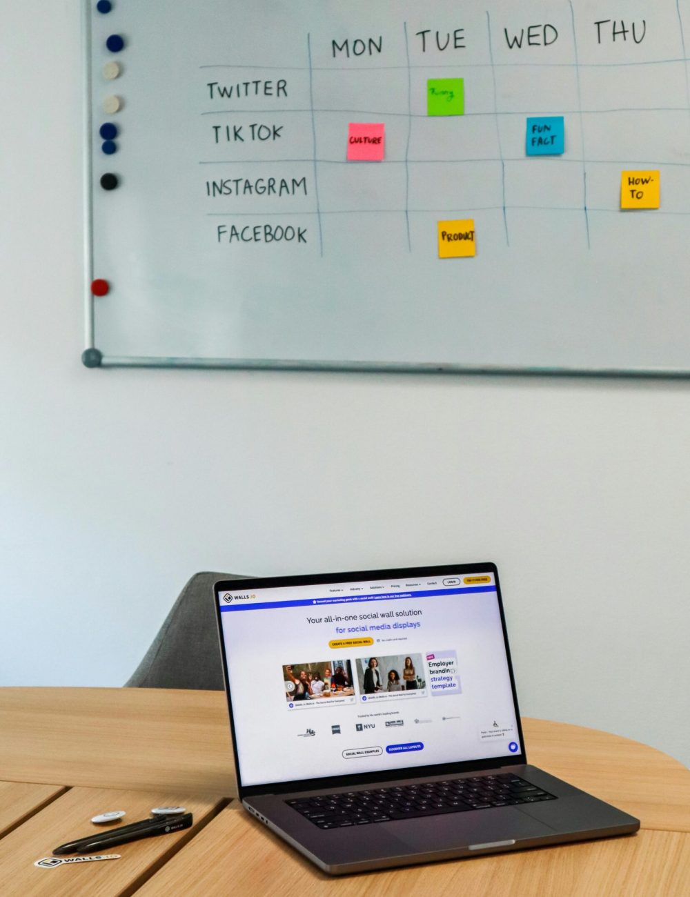 A modern office setup featuring a laptop and a whiteboard schedule for social media platforms.